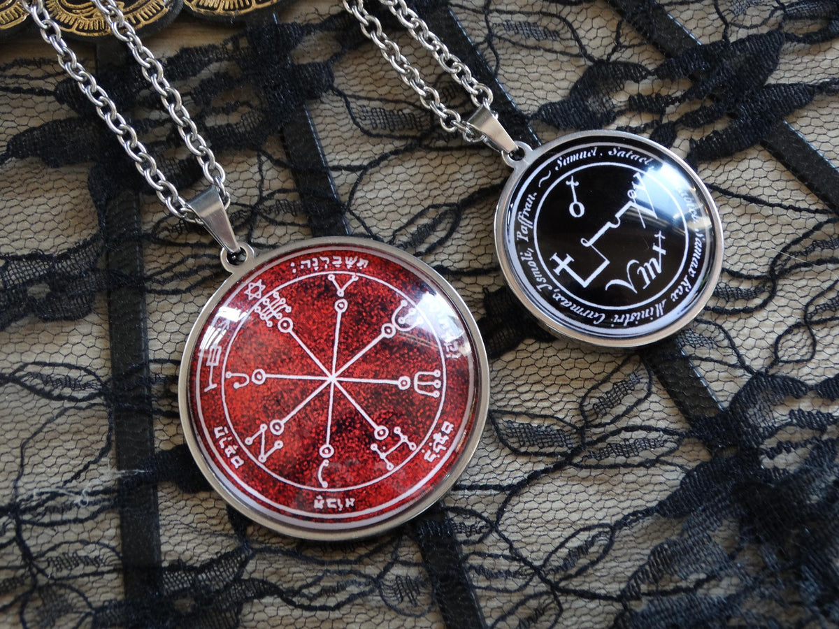 two pendant necklaces with circular designs, one red and one black, hanging on a chain against a black lace background.